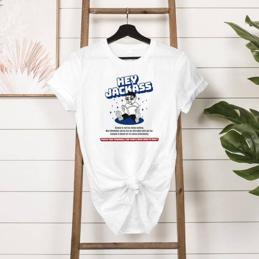 White Hey Jackass T-shirt with bold sarcastic graphic and text, tied at the front, hanging on a wooden ladder against a white shiplap wall.