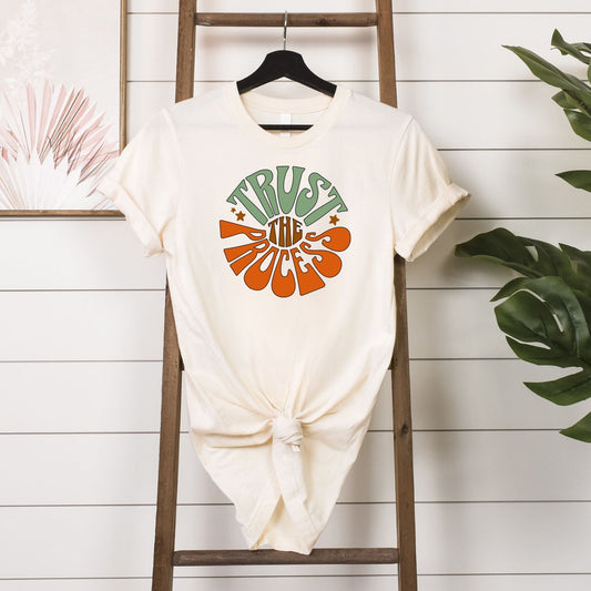 White Trust the Process T-Shirt with retro colorful text design hanging on wooden ladder with plants in background