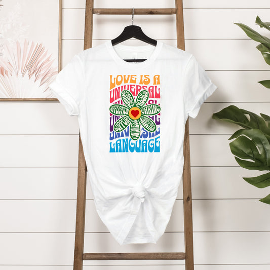 White Love is a Universal Language T-Shirt with colorful flower graphic and positive words displayed on wooden ladder background